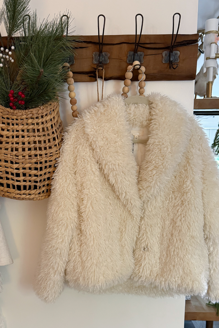 Beige fluffy coat on a coat hanger with a decorative wall in the background